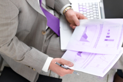 Close up picture of a business man with purple tie, exhaminating some paper with the Analysis result and charts, with a laptop at his side