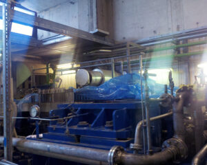 A blue machine in an industrial setting with pipes.